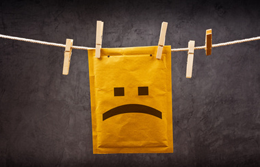 Emotikon tužnog lica na poštanskoj omotnici koja visi na užetu pričvršćenom štipaljkama za odjeću. Koncept loših vijesti.