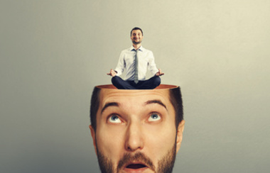 Zadivljeni poslovni čovjek otvorene glave. Mladi smireni poslovni čovjek sjedi u joga asani i smiješi se čovjeku u glavu. Fotografija preko sive pozadine